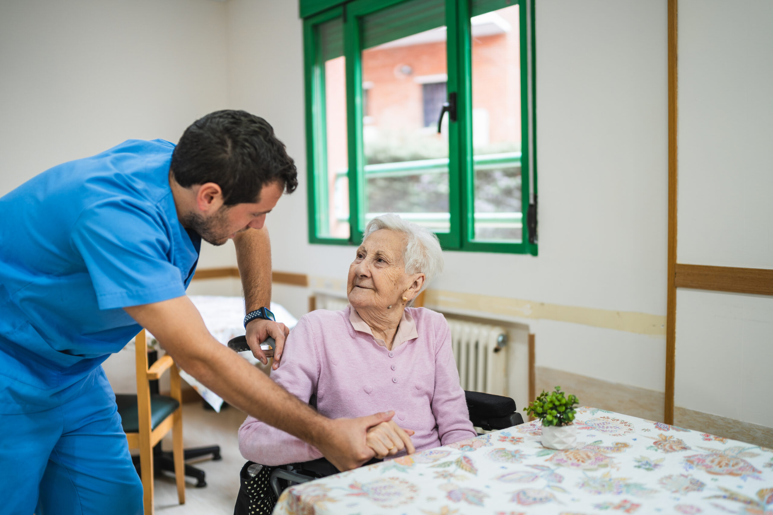 Caregiver assisting senior woman in nursing home Caregiver providing compassionate home health care services for a senior in Hays, KS.
